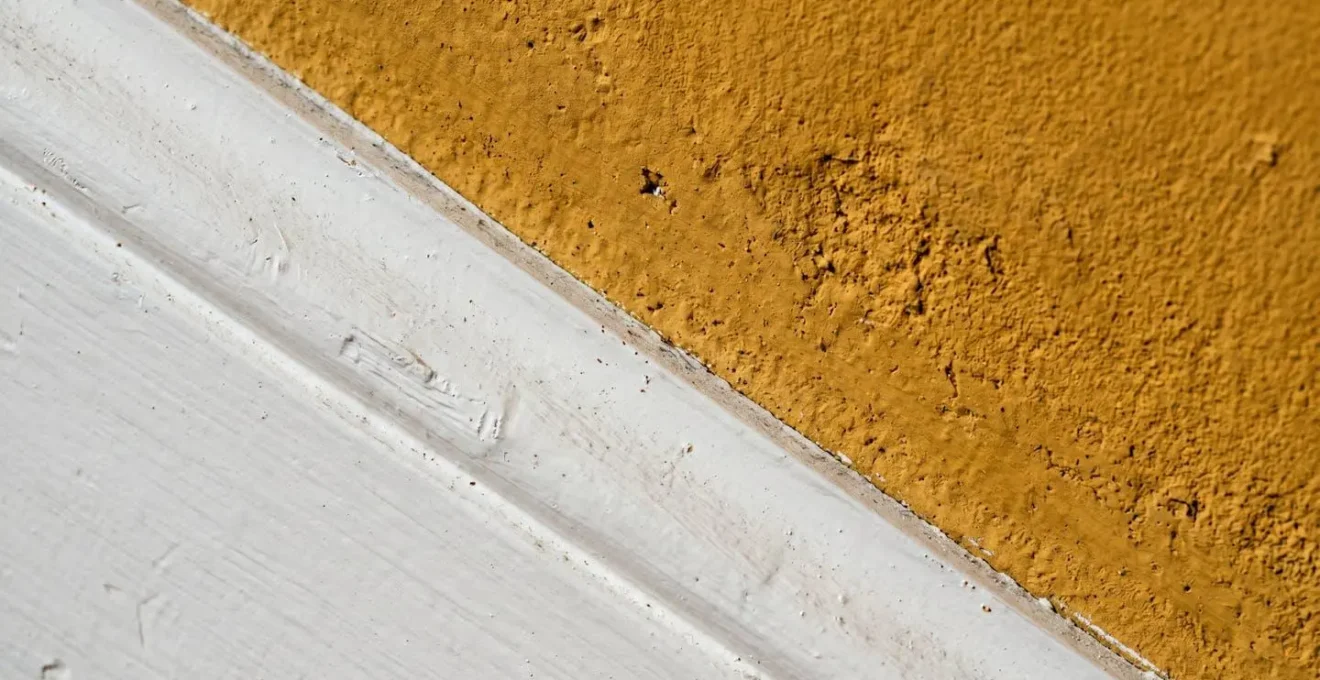 Détail architectural de plinthes blanches sur mur ocre avec jeu de lumière