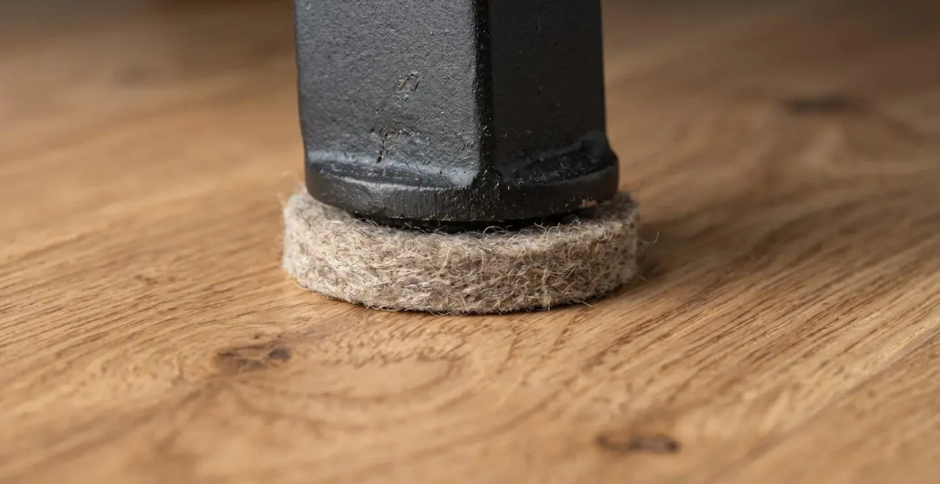 Gros plan sur patins protecteurs en feutre sous pieds métalliques sur parquet en chêne